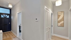 A hallway with a dark door, a light switch, and a painting on the wall. - Spacious 3BR Hawick Apartment, Sleeps 6, Parking (Scottish Borders)