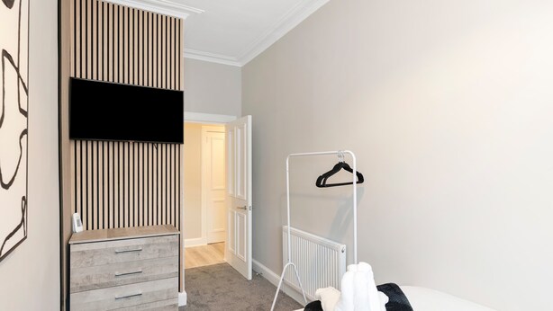 A hotel room with a bed, a wardrobe, a radiator, and a coat rack. - Spacious 3BR Hawick Apartment, Sleeps 6, Parking (Scottish Borders)