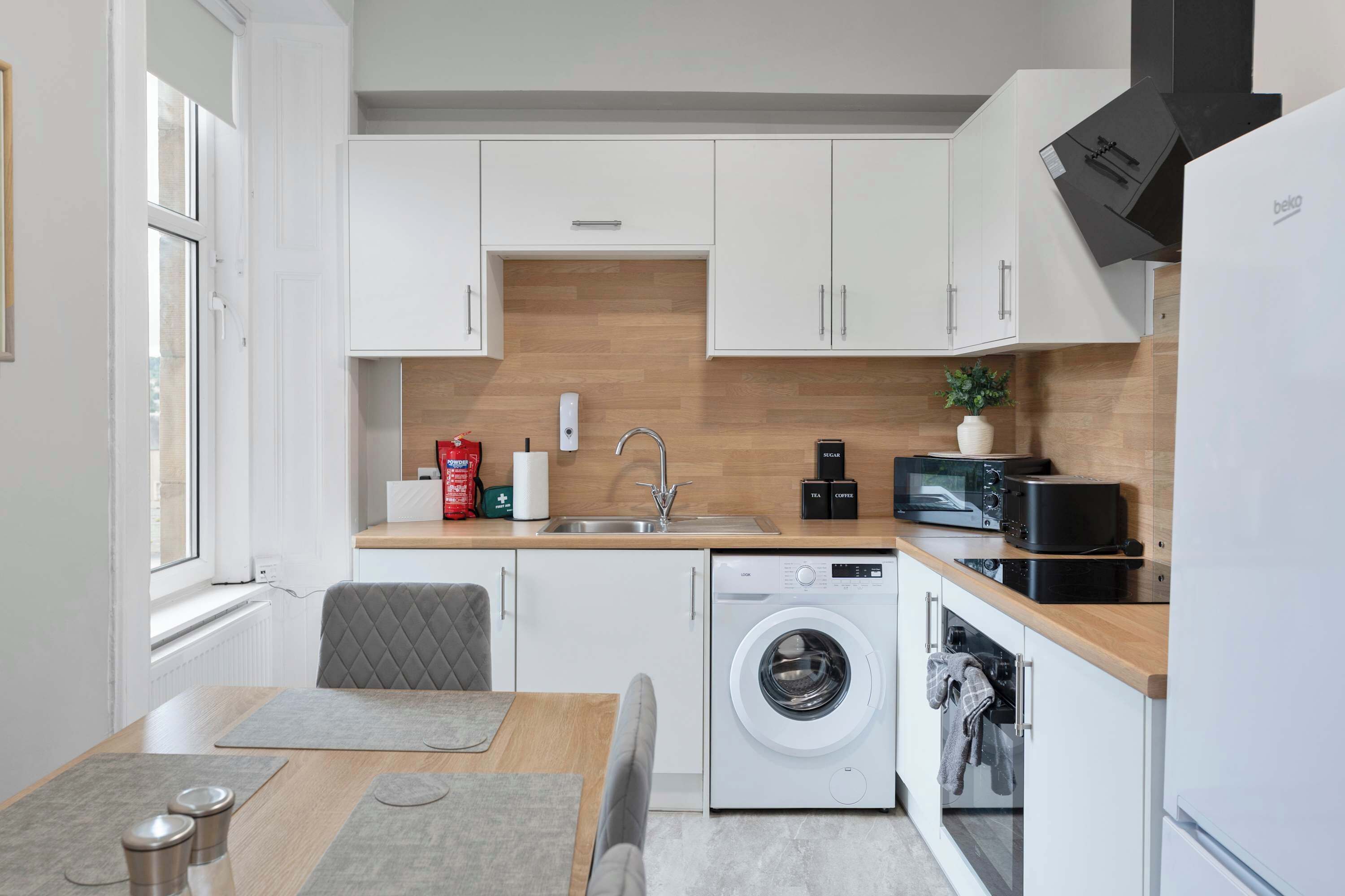 A modern kitchen with white cabinetry, a built-in dishwasher, a washing machine, and a microwave.