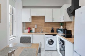 A modern kitchen with white cabinetry, a built-in dishwasher, a washing machine, and a microwave.