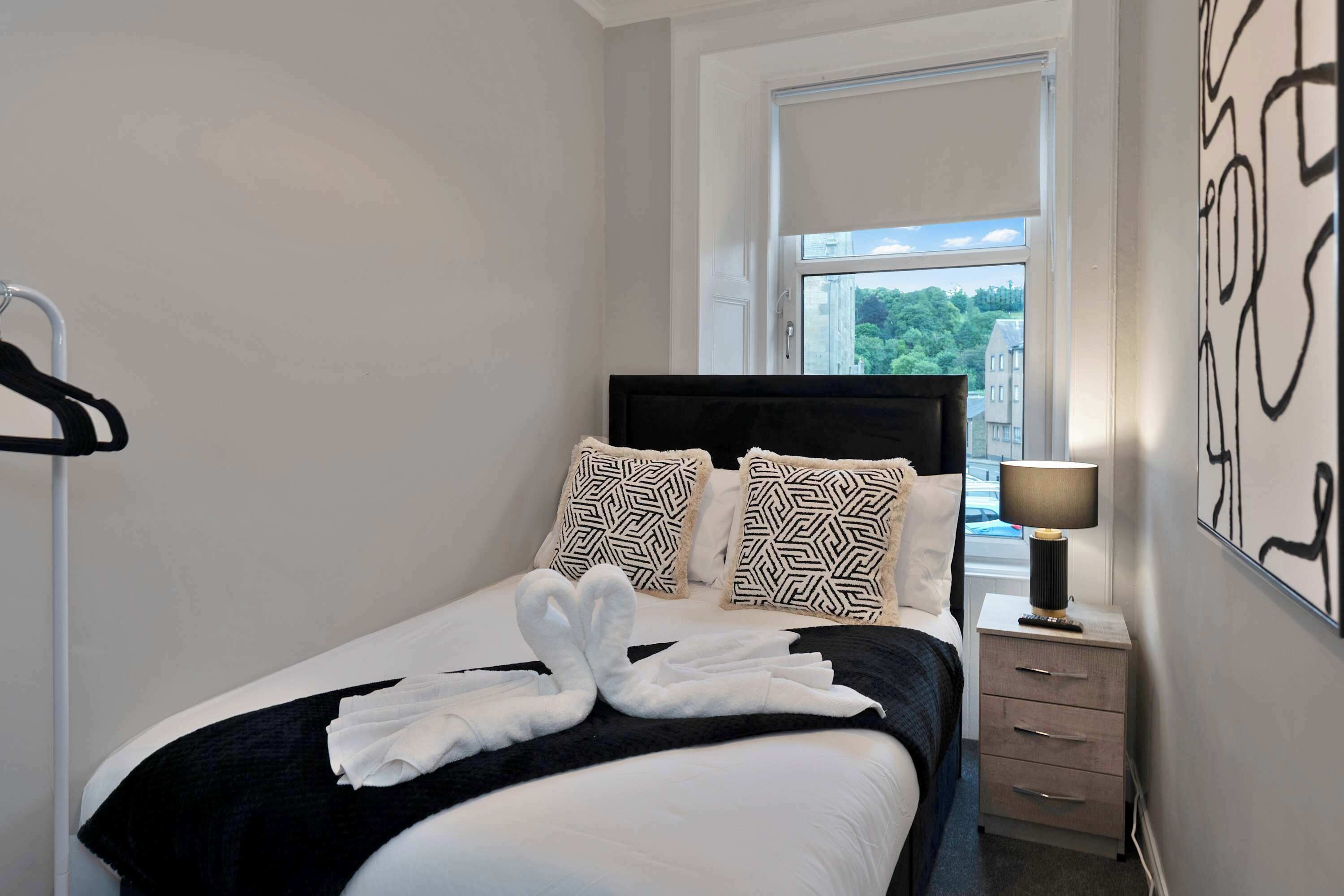 Una cama bien hecha con cabecera negra, ropa de cama blanca y dos almohadas estampadas.