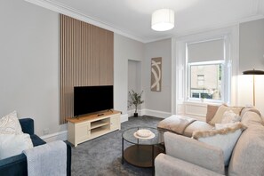 A modern living room with a flat-screen TV, a sofa, a coffee table, and a window with a view.