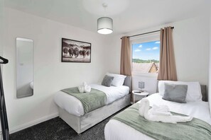 A hotel room with two beds, a large window with curtains, a mounted picture, and a small bedside table. - Contractor Friendly Hawick Apt, Parking, Sleeps 5 (Scottish Borders)