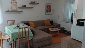 Ein Wohnzimmer mit einer Eckcouch, einem Esstisch mit Stühlen, einem kleinen Beistelltisch und einer Heizung.