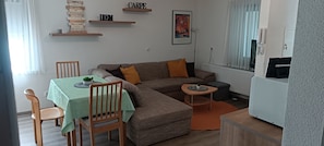 A living room with a sectional sofa, a dining table with chairs, a small side table, and a radiator. - Cozy, modernly furnished vacation rental with a private entrance in an annex (Burgebrach)