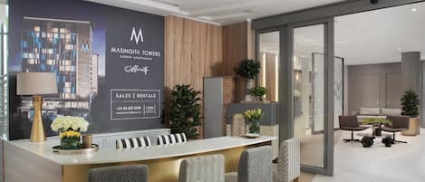 Zona de recepción con mostrador, sillas, planta y pared con logotipo e información de contacto.