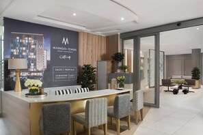 A reception area with a counter, chairs, a plant, and a wall with a logo and contact information. - Newly Upgraded Stays (Sandton)