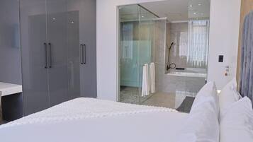 Un dormitorio moderno con una cama grande, un vestidor amplio y un área de ducha con paredes de vidrio.