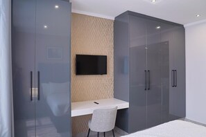 A bedroom with a bed, a desk, a chair, a TV, and wardrobe doors.
