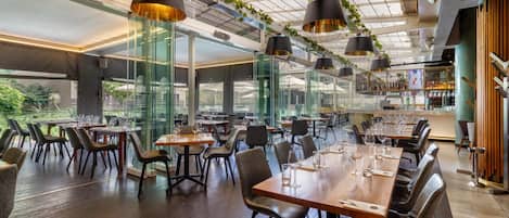 Un restaurant au décor moderne, avec des cloisons en verre, des tables en bois et des chaises noires.