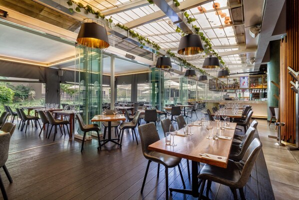 A restaurant with a modern interior, featuring glass partitions, wooden tables, and black chairs.
