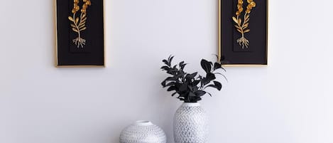 Two framed botanical prints, a white textured vase, and a larger vase with black foliage on a dark wooden table against a white wall.