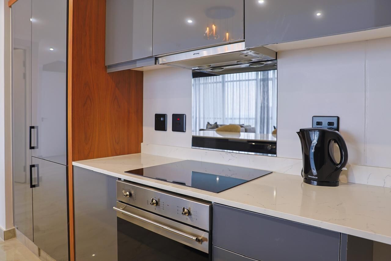 Una cocina moderna con estufa, horno y microondas integrados, un panel de madera decorativo y un hervidor en la encimera.