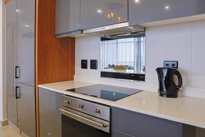 Une cuisine moderne dotée d’une cuisinière, d’un four et d’un micro-ondes encastrés, d’un mur d’accent en bois et d’une bouilloire posée sur le plan de travail.