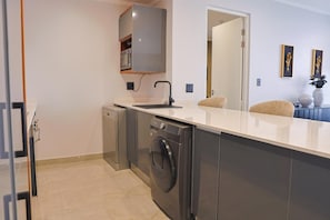 A compact kitchen with a built-in washing machine, a small countertop, and a cabinet above the sink. - Newly Upgraded Stays (Sandton)