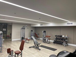 Une salle de sport équipée de divers appareils d’exercice, notamment des bancs, des haltères et des machines de musculation.