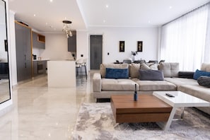 A modern living room with a sofa, coffee table, and a kitchen in the background. - Newly Upgraded Stays (Sandton)