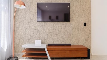 Una habitación moderna con un televisor de pantalla plana montado en una pared texturizada, una mesa blanca con un objeto negro encima y un banco de madera.