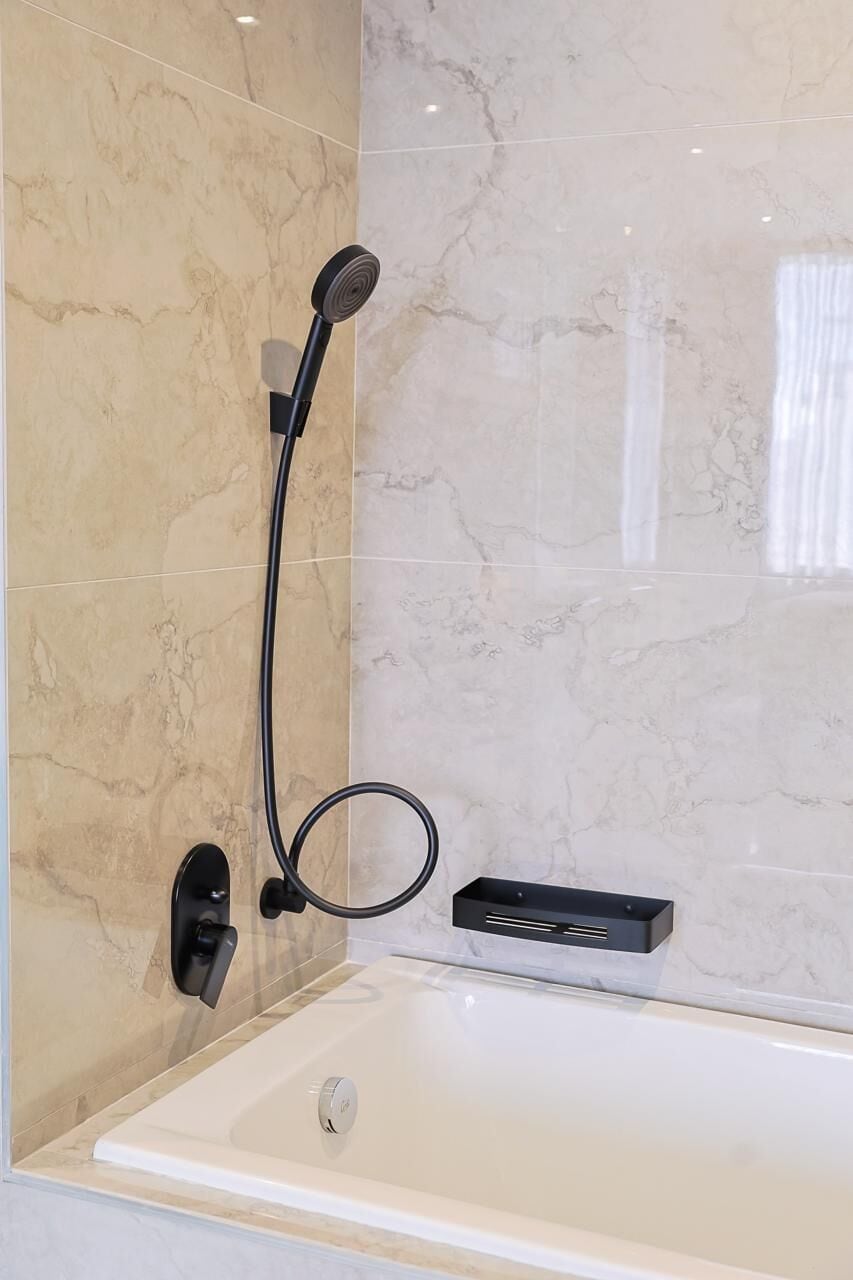 A modern bathroom with a bathtub, a handheld showerhead, and a control panel.