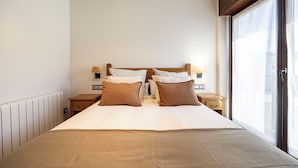 A hotel room with a large bed, two bedside tables with lamps, a radiator, and a window with a view. - La Molina: Ski-in apartment with private parking (Alp)