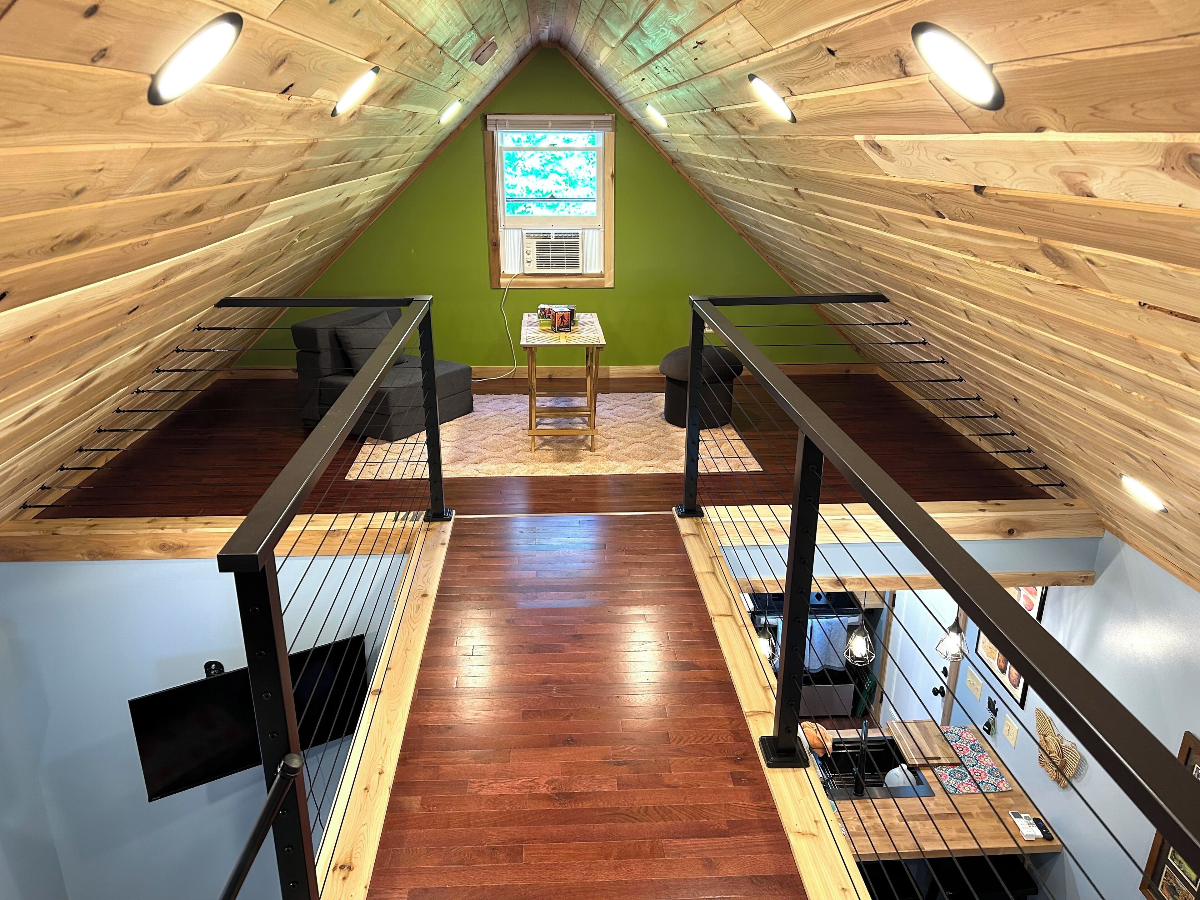A loft-style room with a sloped ceiling, wooden beams, a small table with a chair, and a window with a view.