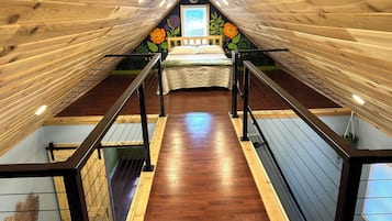 Une chambre avec un plafond en pente, un plancher en bois, un lit recouvert d’une courtepointe blanche et une fresque murale.