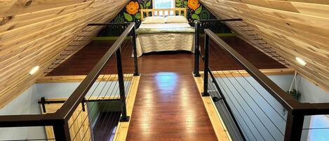 A bedroom with a sloped ceiling, wooden flooring, a bed with a white bedspread, and a wall mural.