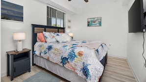 A bedroom with a bed, a nightstand, a ceiling fan, a window with blinds, and a wall-mounted TV. - Home from Home in Heritage Landing Golf Community (Punta Gorda)