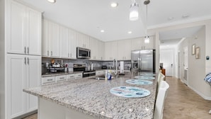 A kitchen with white cabinets, granite countertops, stainless steel appliances, and a central island with placemats. - Home from Home in Heritage Landing Golf Community (Punta Gorda)