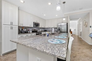 A kitchen with white cabinets, granite countertops, stainless steel appliances, and a central island with placemats.