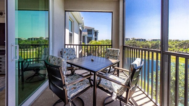 A balcony with a table and chairs, a glass door, and a view of a building and greenery. - Home from Home in Heritage Landing Golf Community (Punta Gorda)