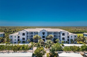 A multi-story hotel with a flat roof, surrounded by palm trees and a view of the ocean.