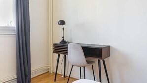 Un espacio de trabajo pequeño y ordenado, con escritorio, silla, lámpara y una ventana con cortinas.