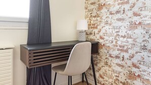 Una habitación con escritorio, silla, lámpara y pared con diseño de ladrillos.