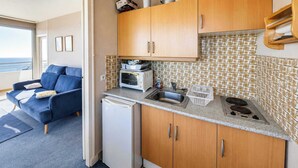 Una kitchenette compacta con microondas, fregadero y estufa, un sofá azul y un refrigerador pequeño.