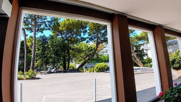 Vista a través de amplios ventanales que muestran un estacionamiento, árboles y un edificio al fondo.