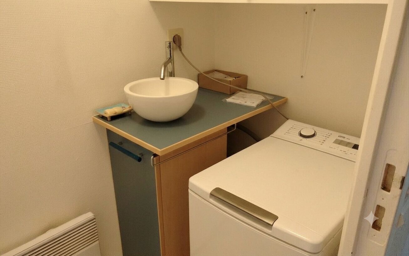 A compact laundry area with a sink, a washing machine, and a small storage box.