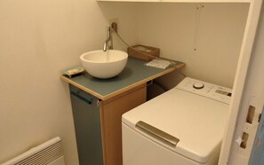 A compact laundry area with a sink, a washing machine, and a small storage box. - Charming house with garden in La Turballe (La Turballe)