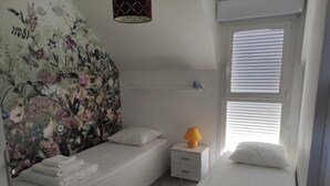 Makuuhuoneessa on kaksi sänkyä, yöpöytä, lamppu ja kukka-aiheinen seinämaalaus.