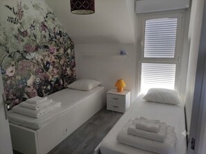 A bedroom with two beds, a nightstand, a lamp, and a floral wall mural. - Charming house with garden in La Turballe (La Turballe)