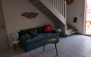 A living room with a blue sofa, a small table, a fan, and a staircase. - Charming house with garden in La Turballe (La Turballe)