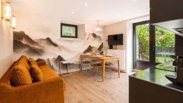 A modern living room with a sofa, a dining table, and a TV mounted on the wall. - Studio with south terrace & Mont Blanc view (Chamonix-Mont-Blanc)