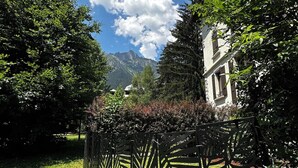 A garden with a patterned fence, a building with a white facade, and mountains in the background. - Studio with south terrace & Mont Blanc view (Chamonix-Mont-Blanc)