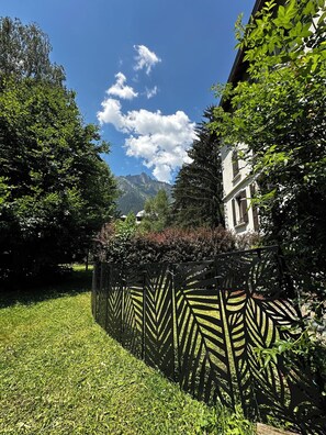 Ein Garten mit Zierzaun, ein Gebäude mit weißer Fassade und Berge im Hintergrund.