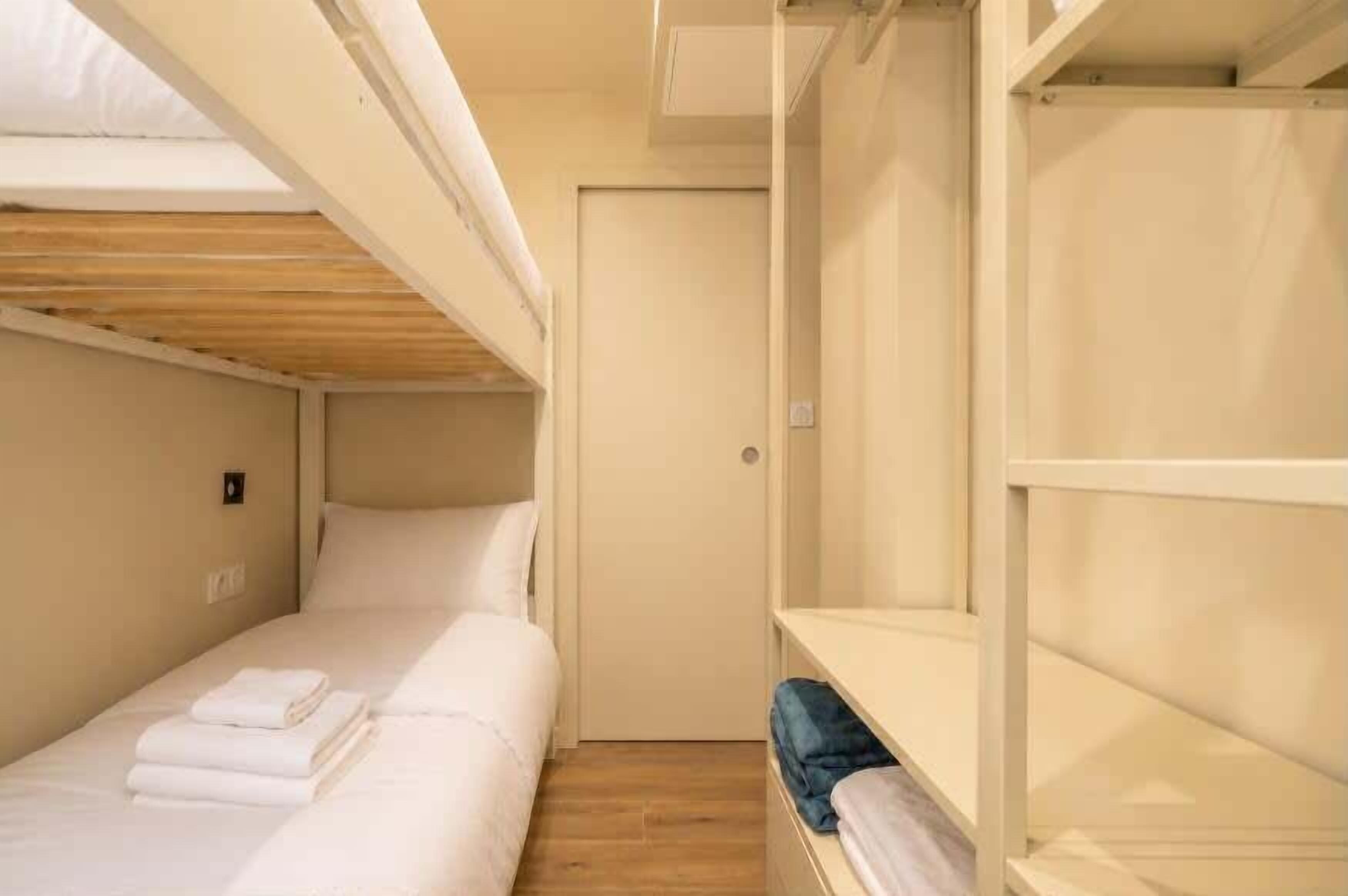 Habitación con literas, una pequeña estantería y techo de madera.