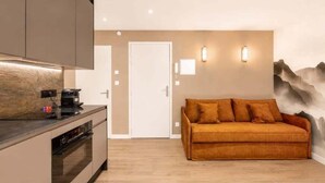 A modern kitchen with a built-in oven and a coffee machine, a sofa with cushions, and a wall-mounted light fixture. - Studio with south terrace & Mont Blanc view (Chamonix-Mont-Blanc)