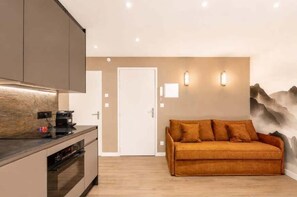 Eine moderne Küche mit Einbauofen und Kaffeemaschine, eine Couch mit Kissen und einer Wandleuchte.