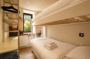 Ein Schlafraum mit Etagenbett, Fenster, Heizkörper und einer Wandleuchte.