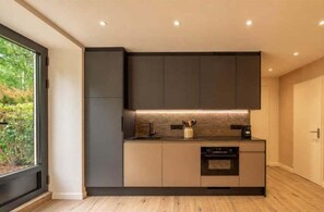 A modern kitchen with dark cabinetry, a built-in oven, and a window providing a view of greenery outside. - Studio with south terrace & Mont Blanc view (Chamonix-Mont-Blanc)