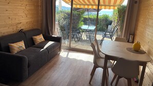 A room with a sofa, a dining table, and chairs, a sliding glass door leading to an outdoor area with a table and chairs, and a yellow bell pepper on the table. - Studio with sea view, terrace and shared pool (Sainte-Maxime)